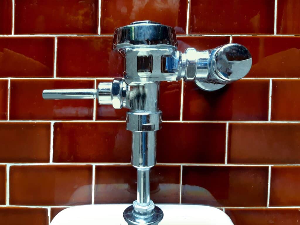 Forkromet VVS-skylleventil til toilet monteret mod rødbrun flisevæg af Mankov VVS