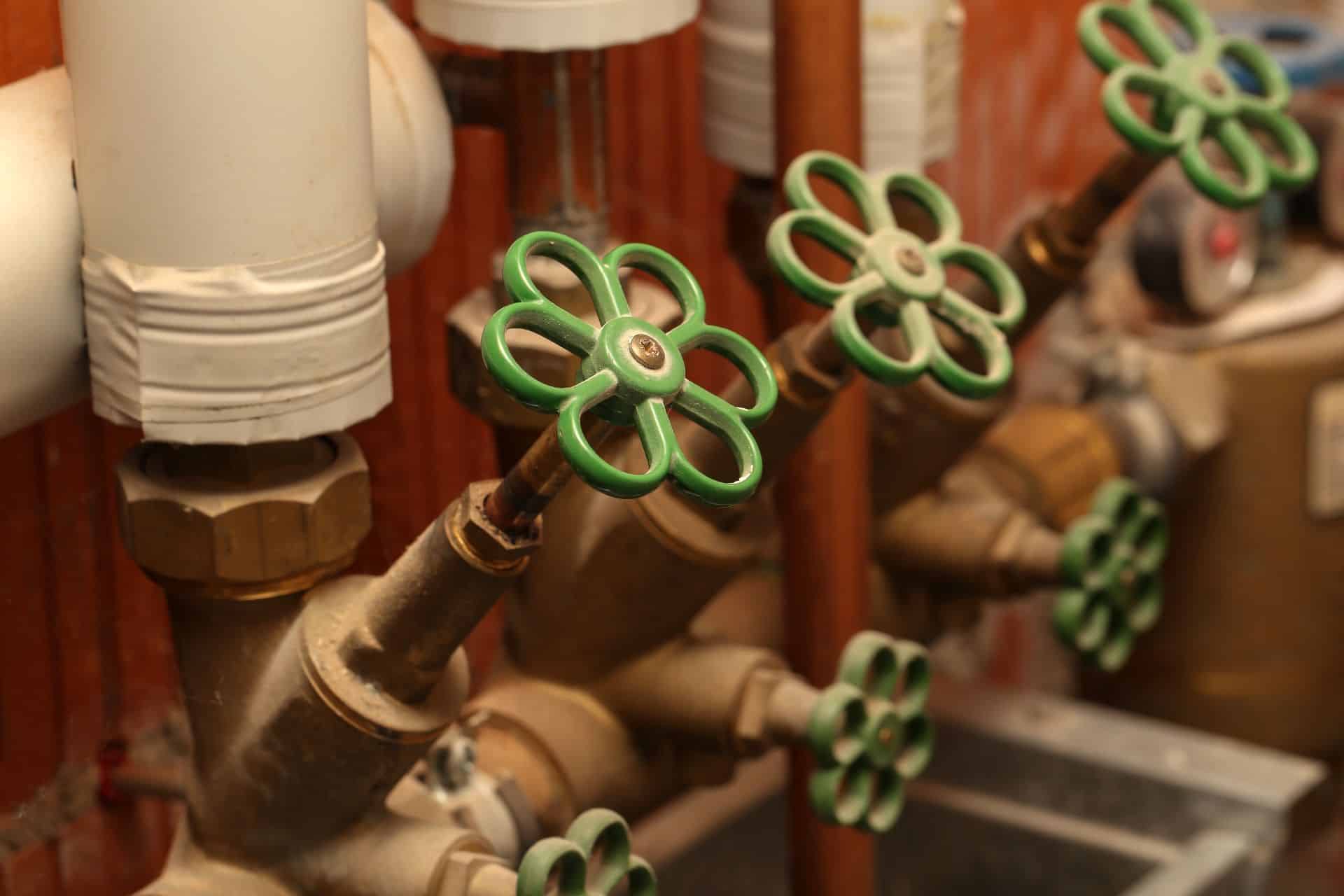 VVS-installation med grønne ventilhåndtag på varmerør i fyrrum